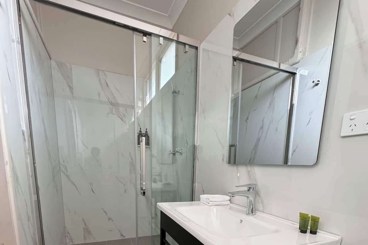 Une salle de bain avec une douche à parois de verre, un lavabo blanc doté d’un cadre noir et un miroir au-dessus du lavabo.