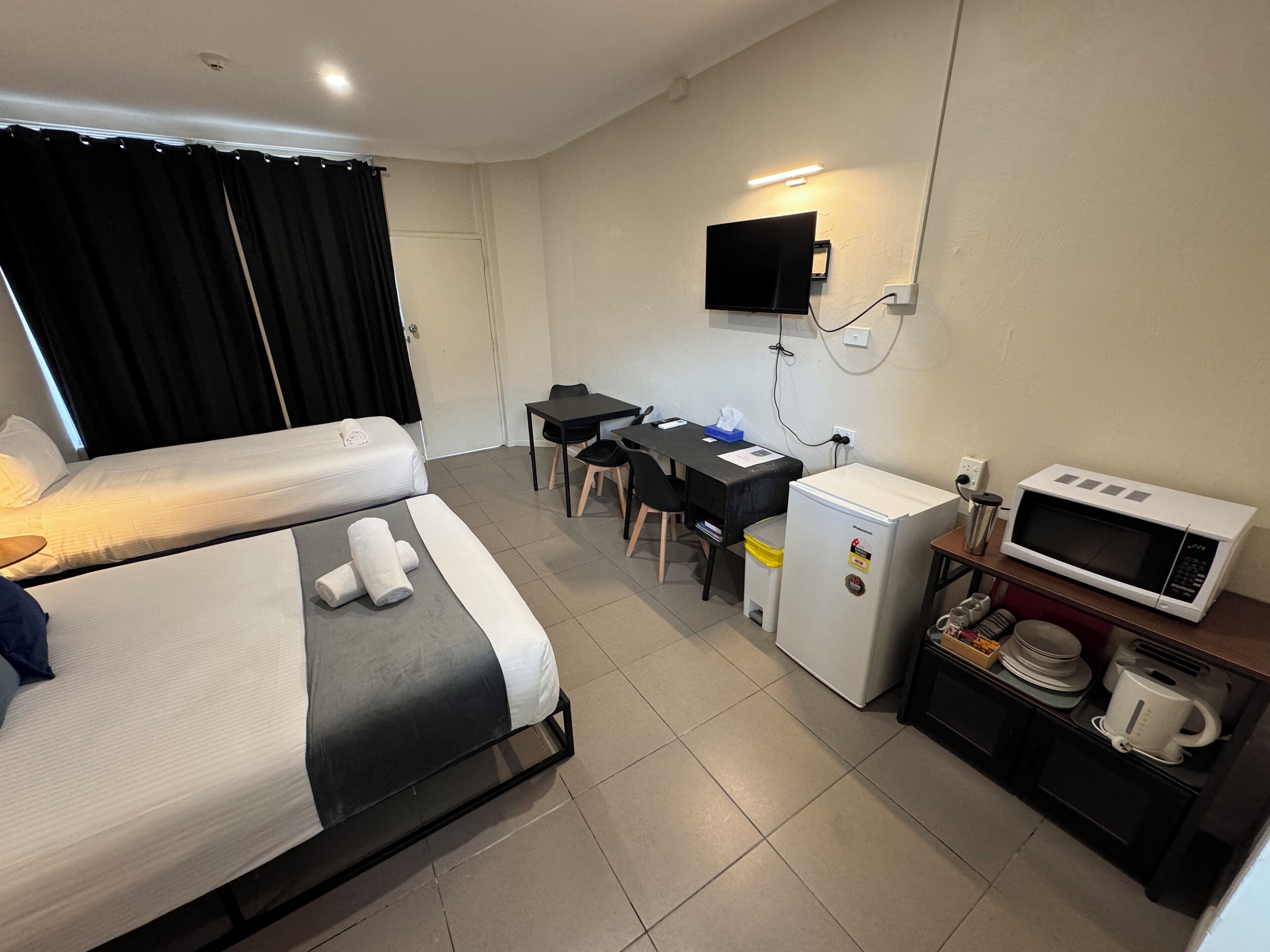 A hotel room with two beds, a desk, a TV, a microwave, and a small kitchenette.
