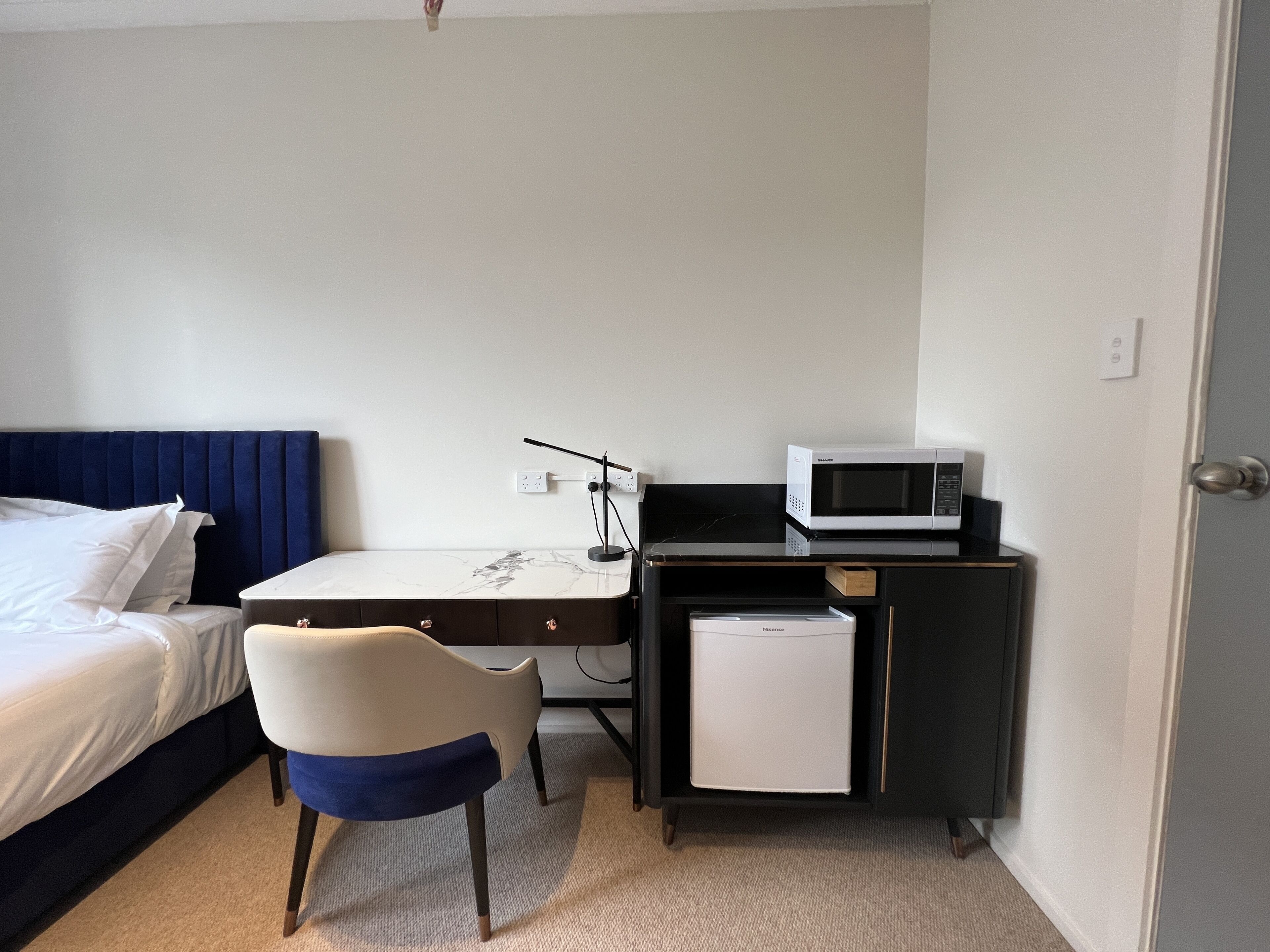 A hotel room with a bed, a desk with a chair, a microwave, and a small refrigerator.