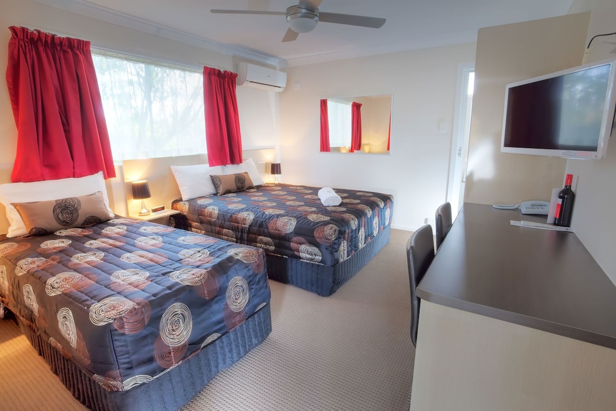 Habitación de hotel con dos camas, un escritorio, un televisor y un ventilador de techo.