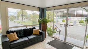A reception area with a black leather sofa, a wooden table, and a large window offering a view of the parking lot and greenery outside.