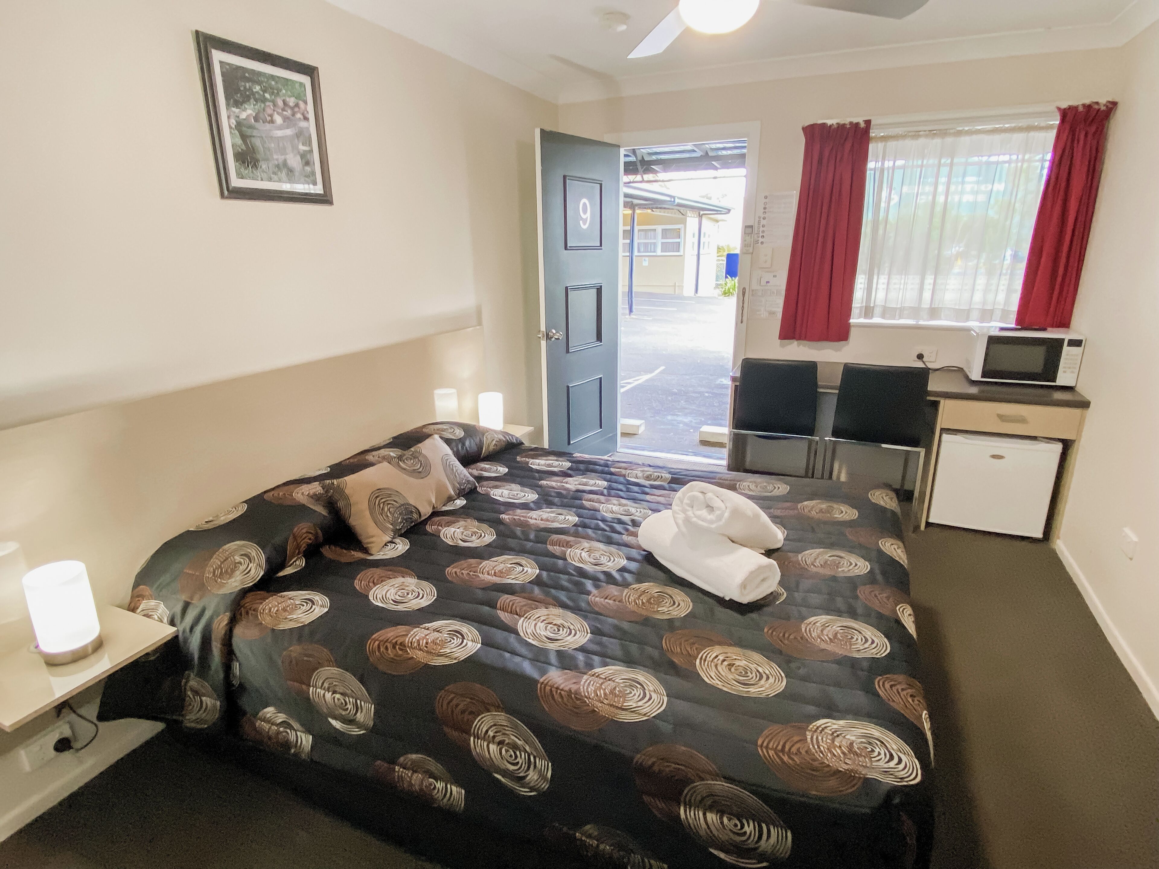 A hotel room with a bed, a desk, a chair, a microwave, and a refrigerator.