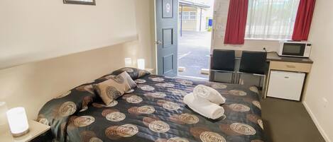 A hotel room with a bed, a desk, a chair, a microwave, and a refrigerator.