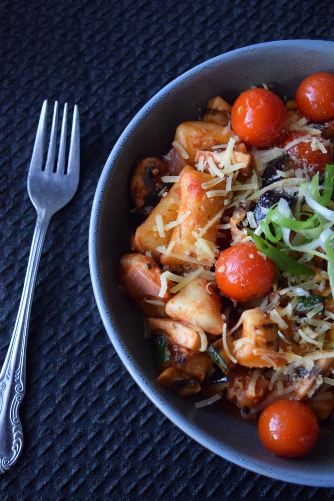 A bowl of pasta with cherry tomatoes and cheese on a textured surface.