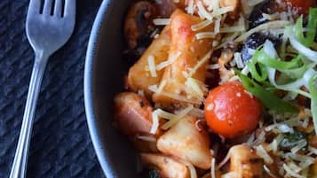 A bowl of pasta with cherry tomatoes and cheese on a textured surface.