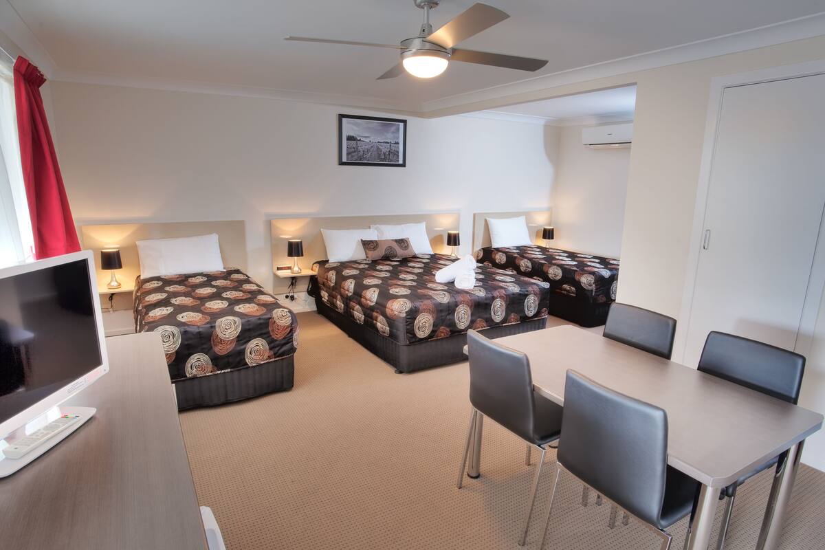 A hotel room with two beds, a TV, a desk, and a ceiling fan.