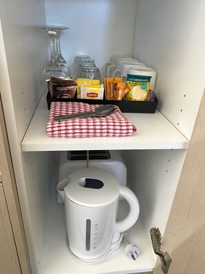 Un área de cocina con una tetera, una cafetera, una tetera de té y varios alimentos en un estante.