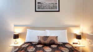 A neatly made bed with a patterned bedspread, two bedside lamps, and a framed picture above the bed.