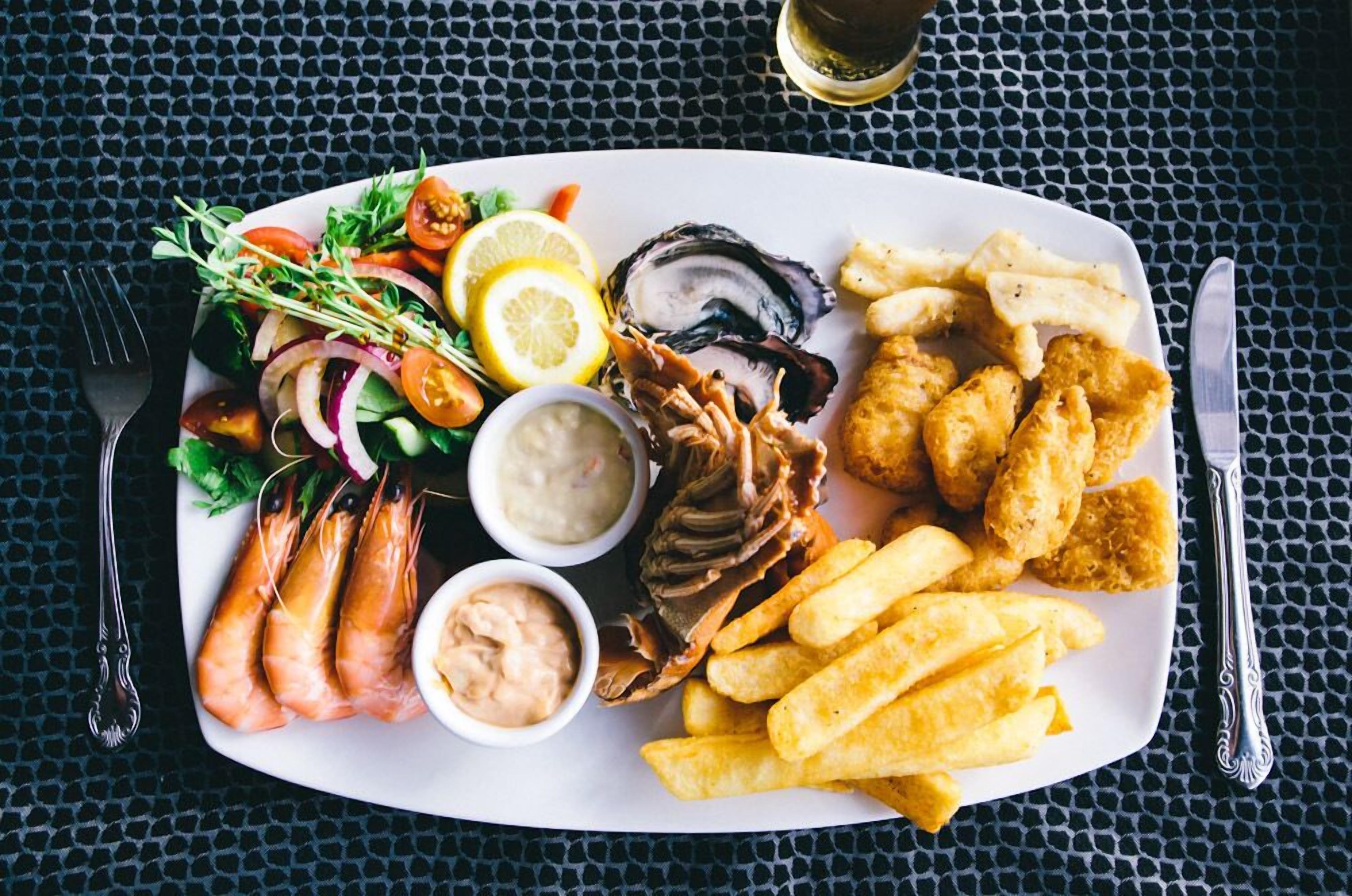 A seafood platter with shrimp, oysters, and fries on a white plate.