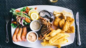 Una bandeja de mariscos con camarones, ostras y papas fritas sobre un plato blanco.