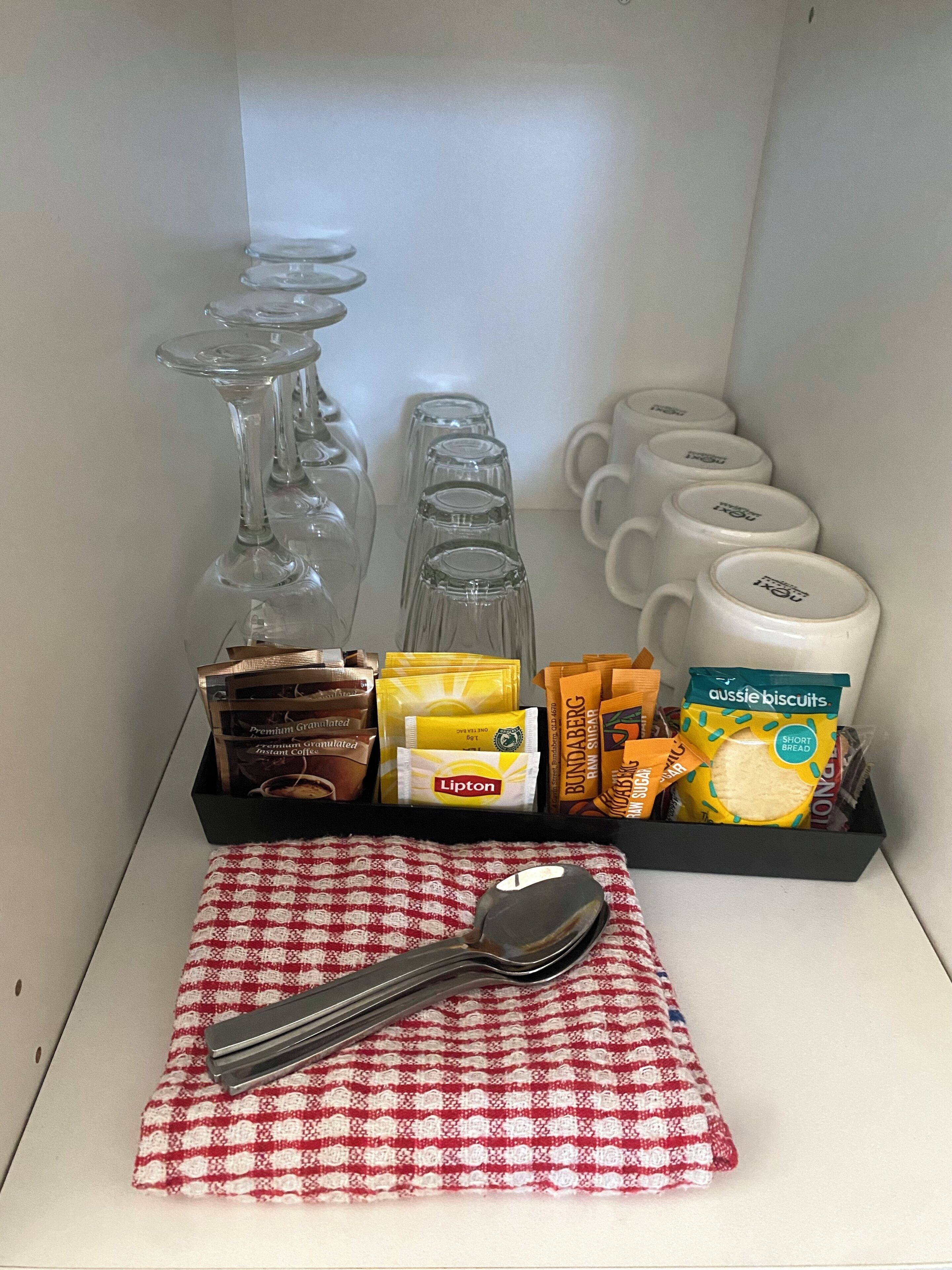 A tray with various food items and a spoon on a red and white checkered napkin.