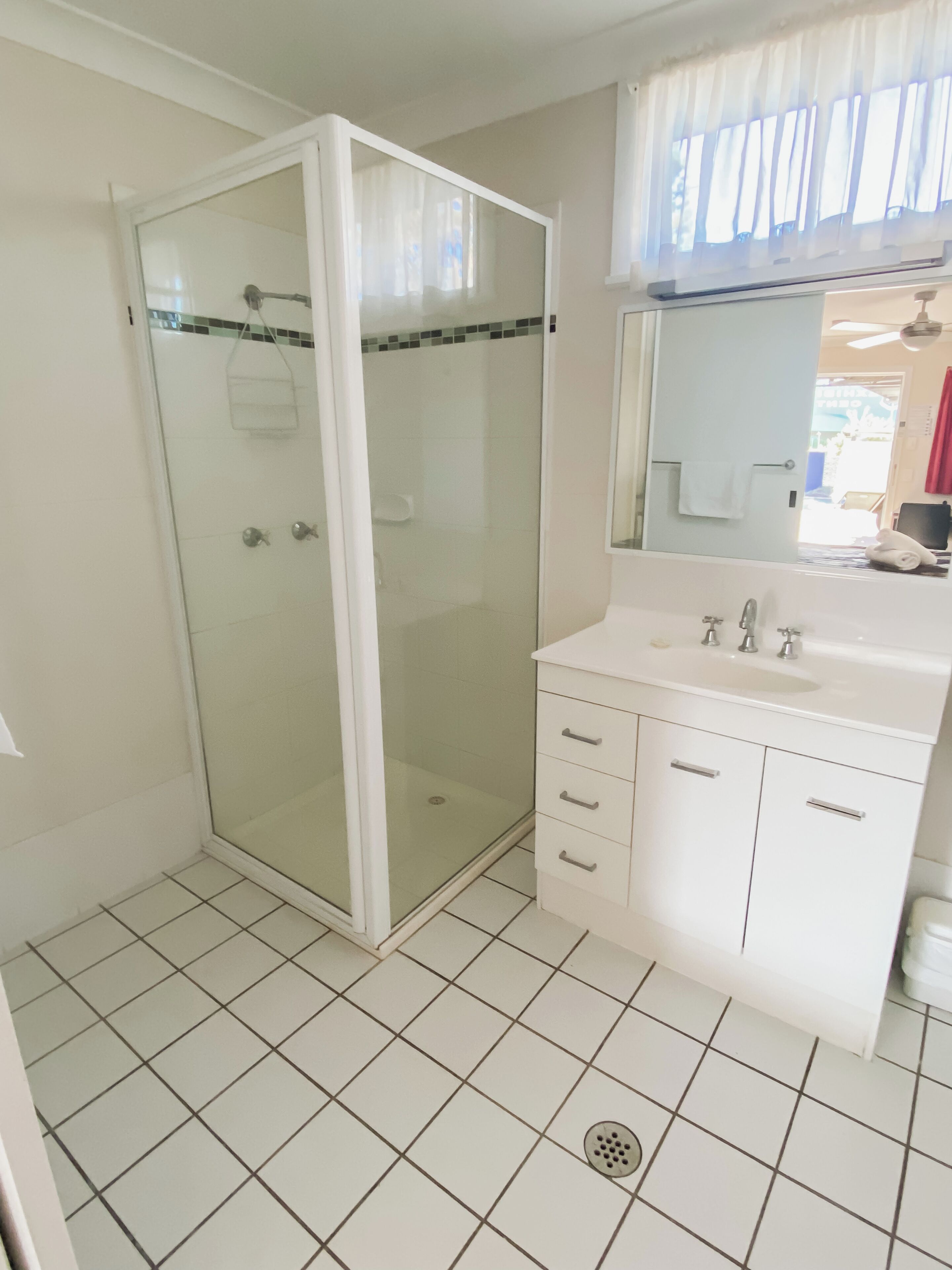 Une salle de bain avec une douche à parois de verre, un lavabo blanc doté de deux robinets et un miroir au-dessus du lavabo.