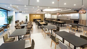 A modern restaurant with multiple dining tables and chairs, a kitchen area, and a large screen displaying a menu. - Hotel Bellclassic Tokyo (Tokyo)