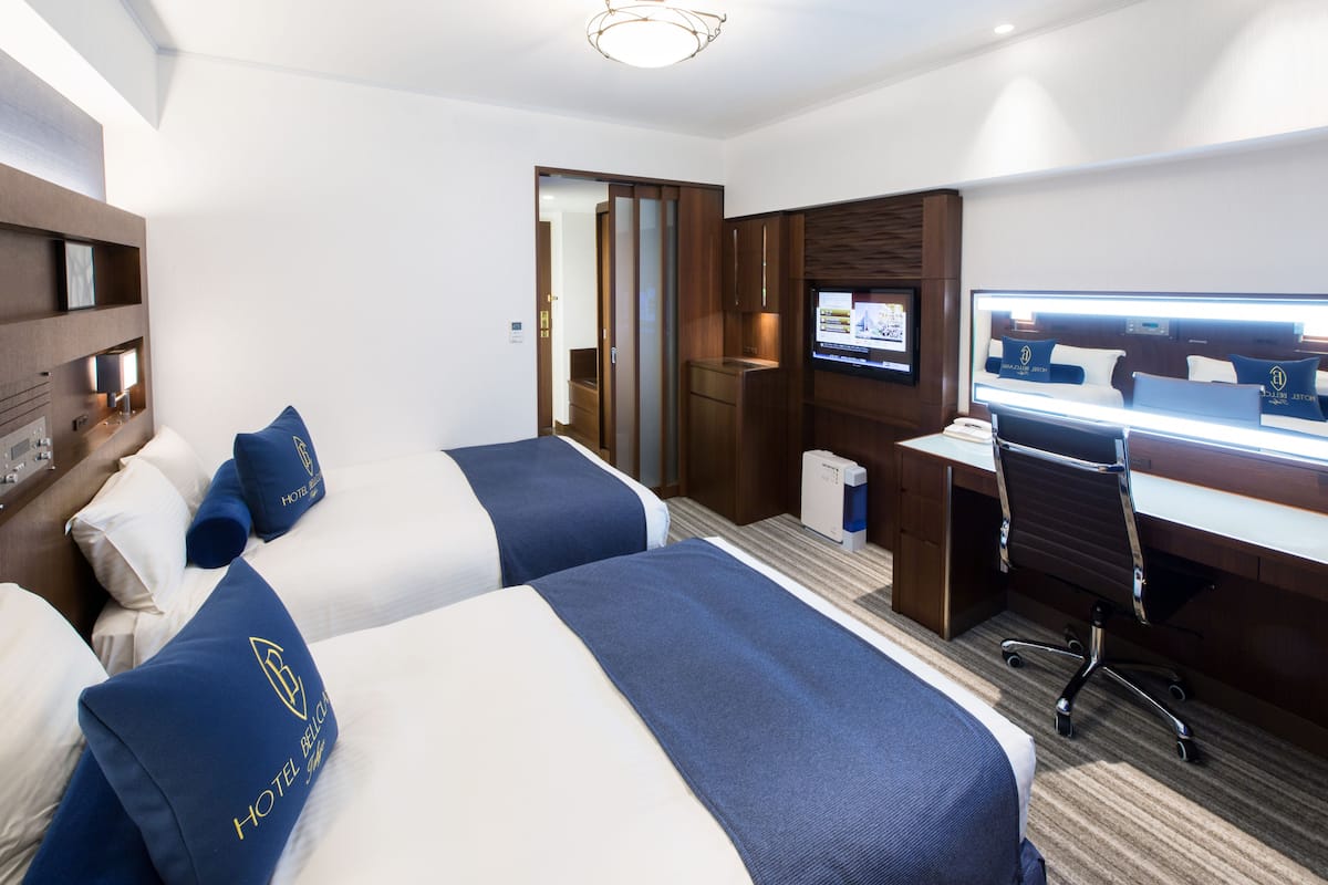 A hotel room with two beds, a desk, a chair, a TV, and a minibar.