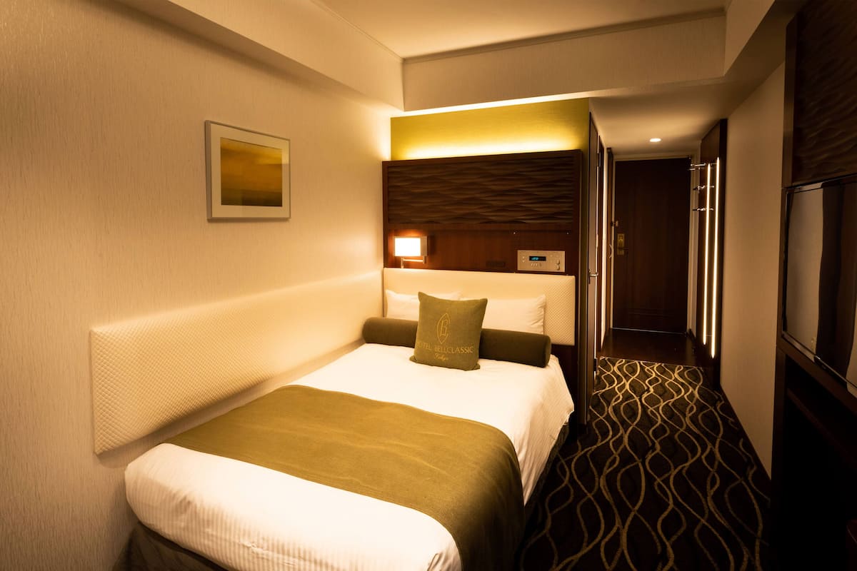 A hotel room with a large bed, a bedside table, a lamp, and a view of the hallway.