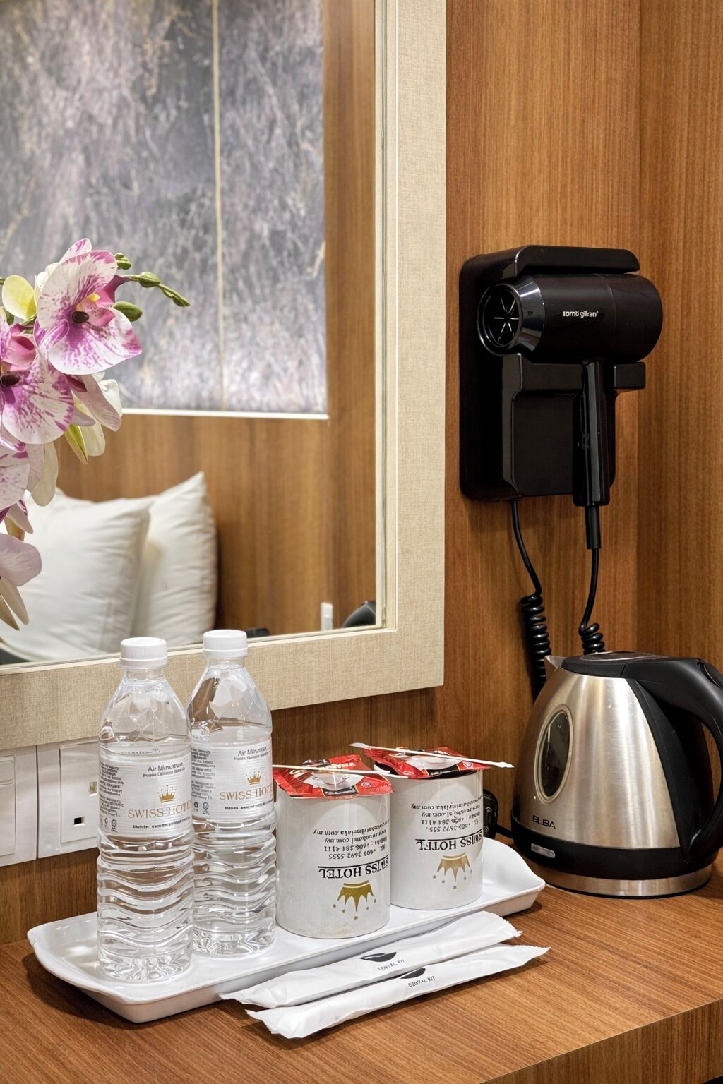 A hotel room with a mirror, a hair dryer, a kettle, and amenities including bottled water and coffee.