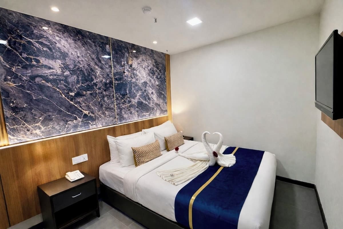 Een moderne hotelkamer met een grote marmeren wand, een netjes opgemaakt bed met een blauw-gouden sprei, en een houten nachtkastje met een telefoon en een klein lade.