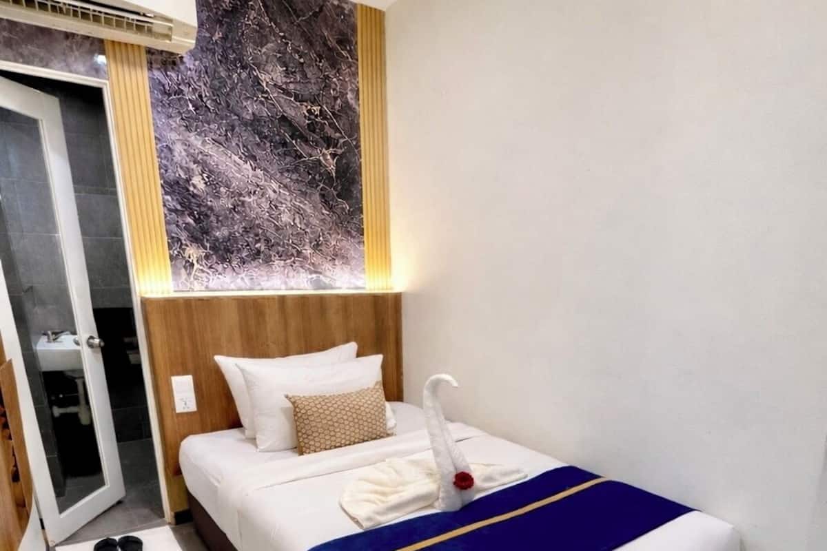 Hotelkamer met een bed, een houten hoofdbord, een wandairconditioner, een wit vloerkleed en een klein bureau.