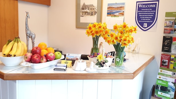A reception desk with a fruit bowl, a framed picture, a welcome sign, and travel guides. - Fitzherbert Castle Motel (Palmerston North)