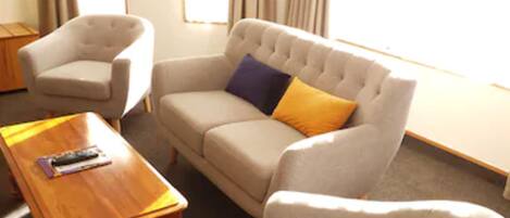 Una sala de estar con un sofá, dos sillones, una mesita de centro de madera y una pequeña mesa auxiliar.