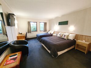 A hotel room with two beds, a desk, a chair, a TV, and a window with curtains. - Fitzherbert Castle Motel (Palmerston North)