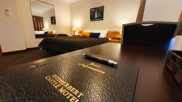 Habitación de hotel con cama, escritorio con bolígrafo, lámpara y un cuadro en la pared.