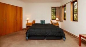A bedroom with a large bed, wooden wardrobe, two bedside tables with lamps, and a window with curtains. - Fitzherbert Castle Motel (Palmerston North)