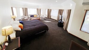 A hotel room with a large bed, a desk with a lamp, two armchairs, a sofa, and a TV. - Fitzherbert Castle Motel (Palmerston North)