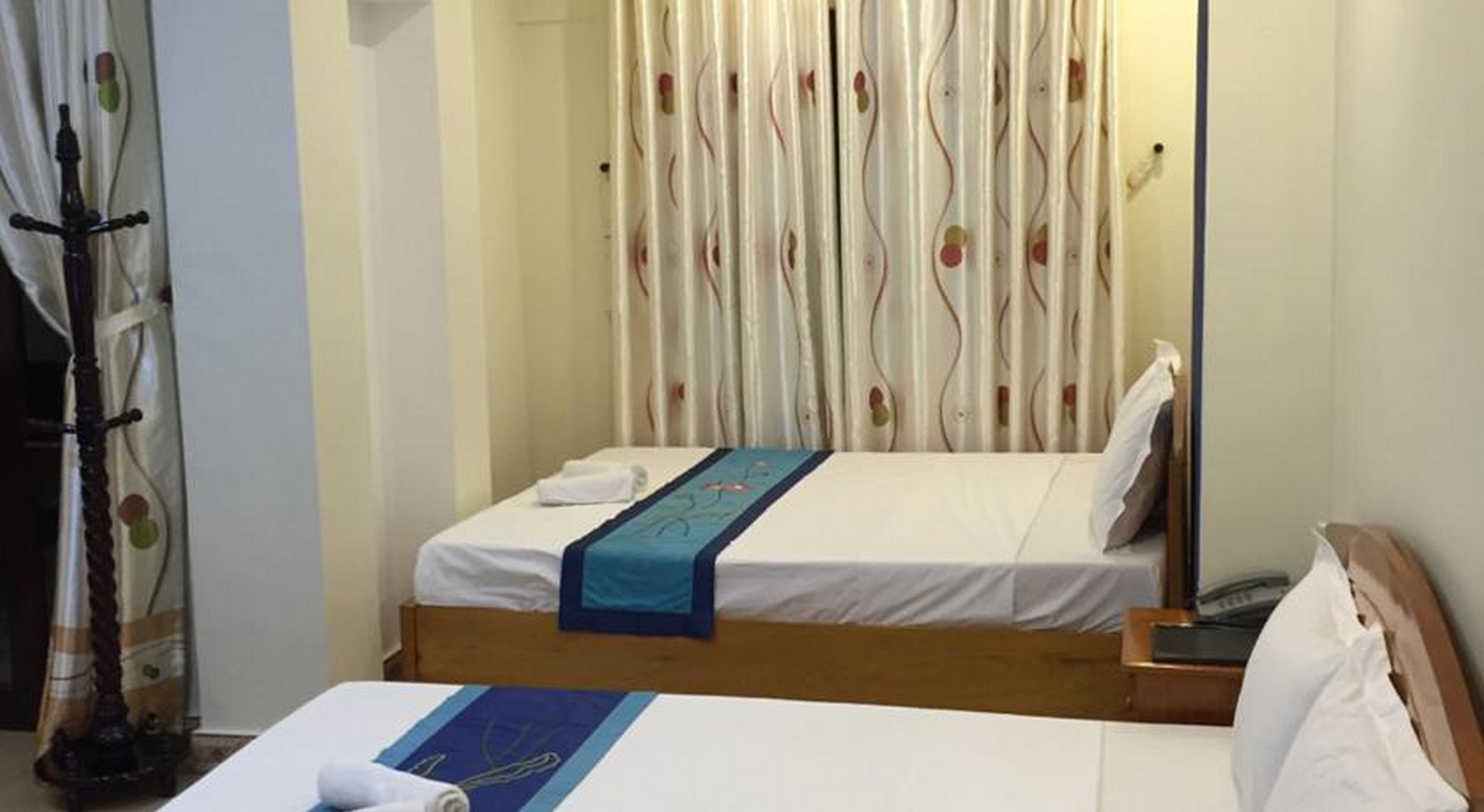 A hotel room with a bed, a wooden headboard, a bedside table, and a curtain with a wavy pattern.