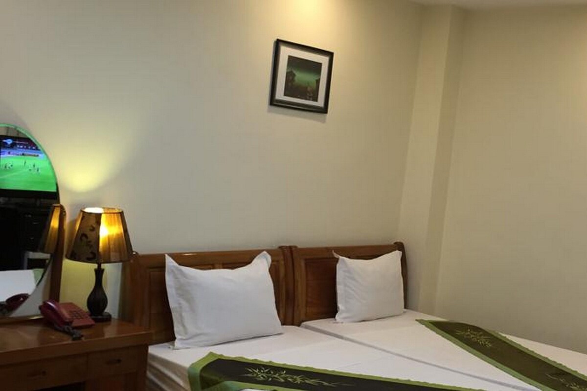 A hotel room with a bed, two bedside lamps, a small framed picture on the wall, and a desk with a telephone and a lamp.