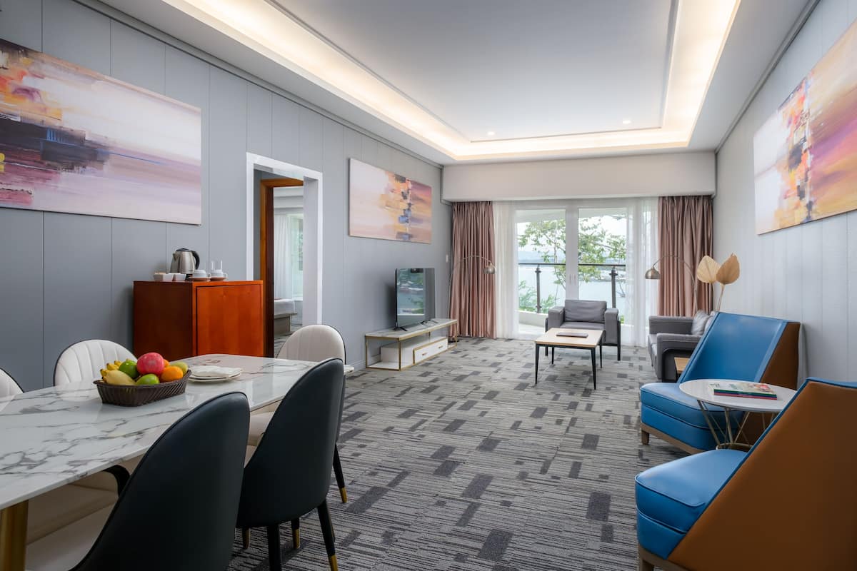 Habitación de hotel con zona de comedor, televisor y balcón con cortinas.