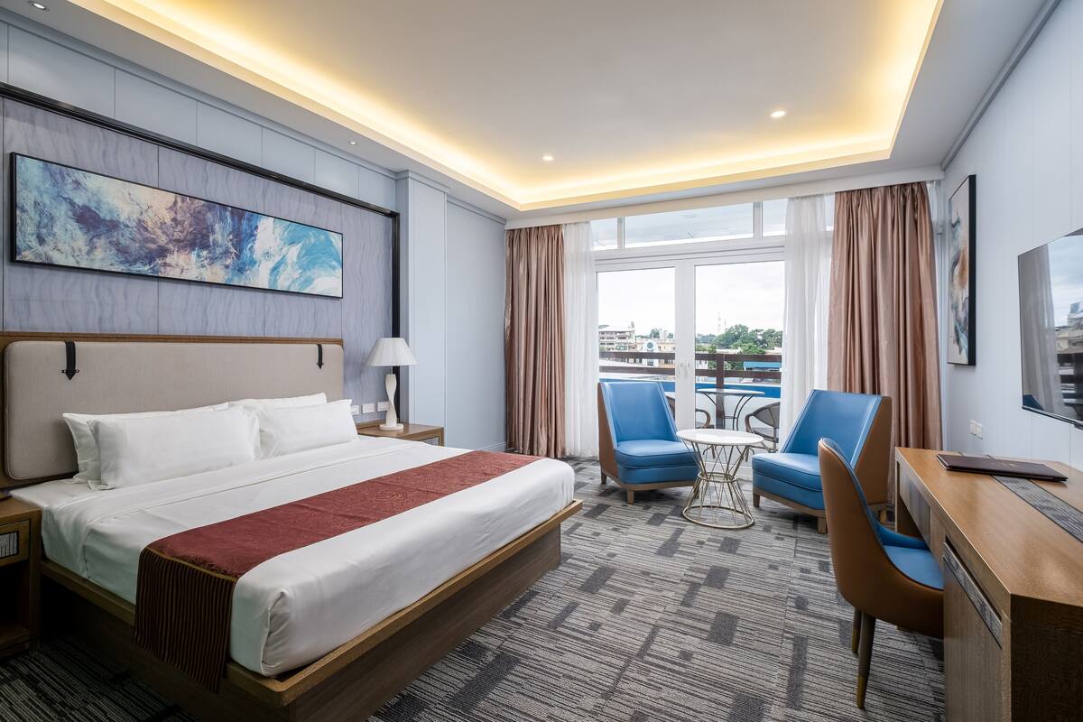 Una habitación de hotel con una cama grande, un escritorio con silla, una mesita y un televisor.