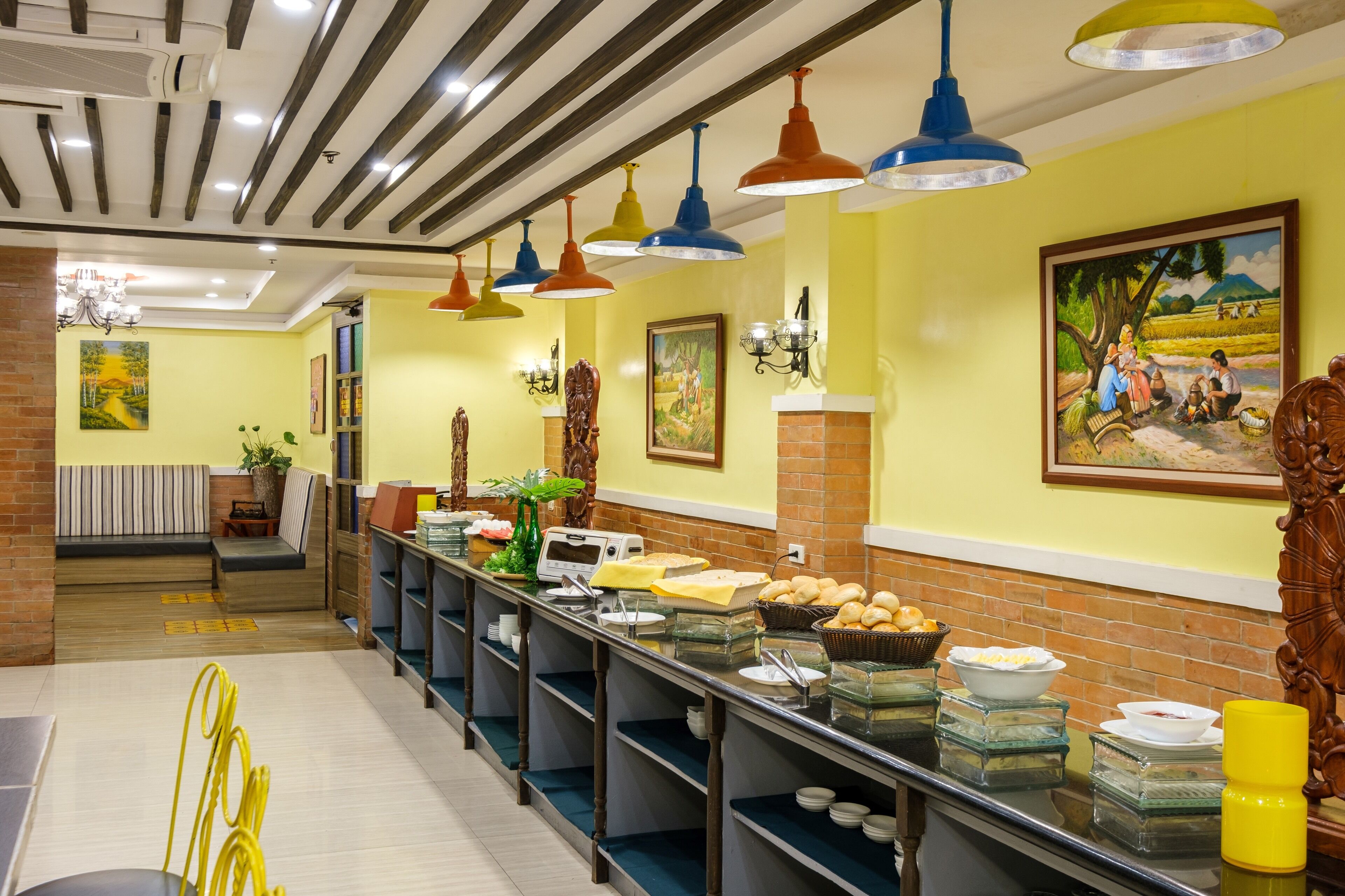 A buffet area with a variety of food items, a seating area with a bench, and a painting on the wall.