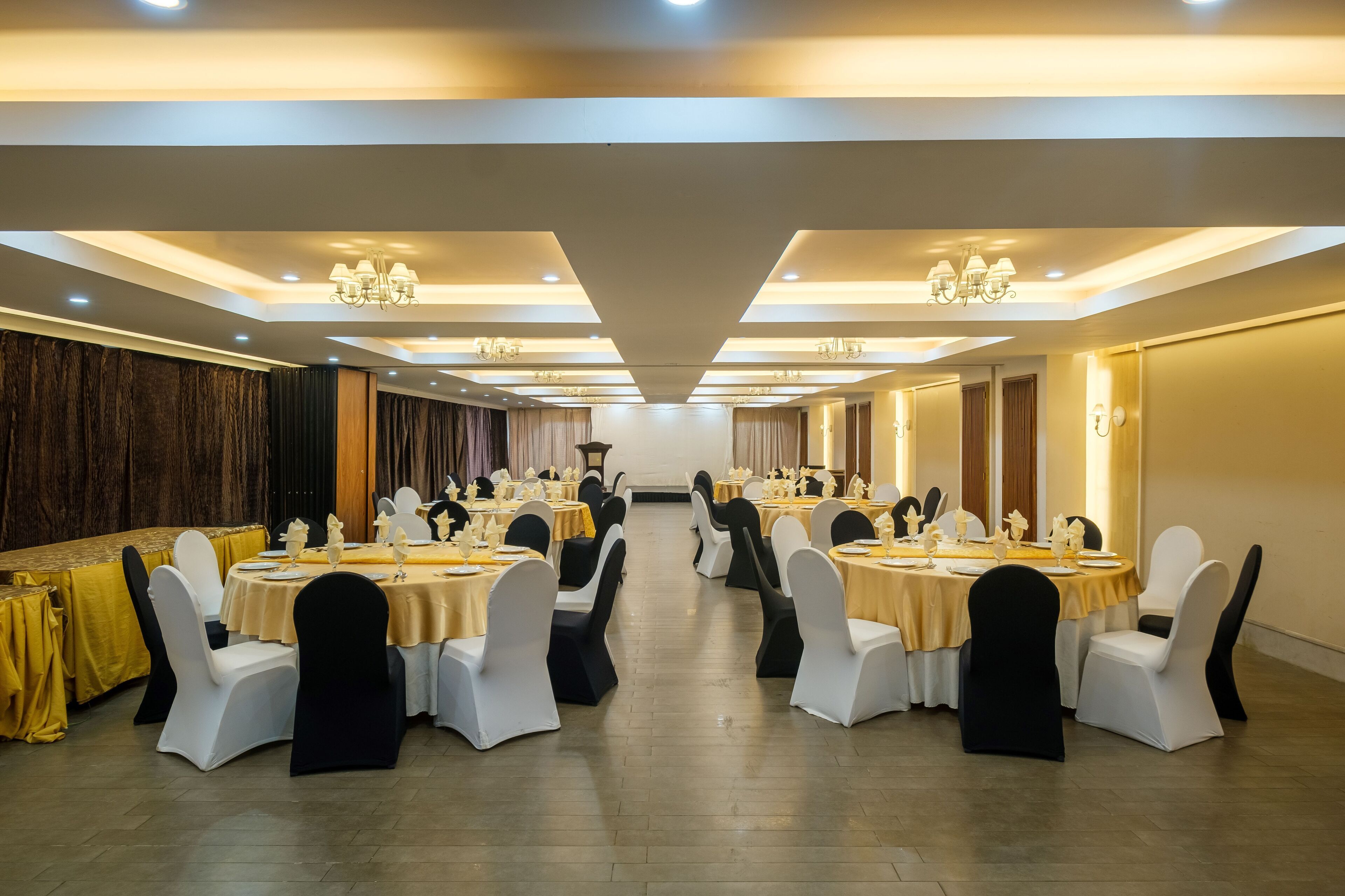 Un salón de banquetes con mesas redondas, sillas negras y blancas, y candelabros.