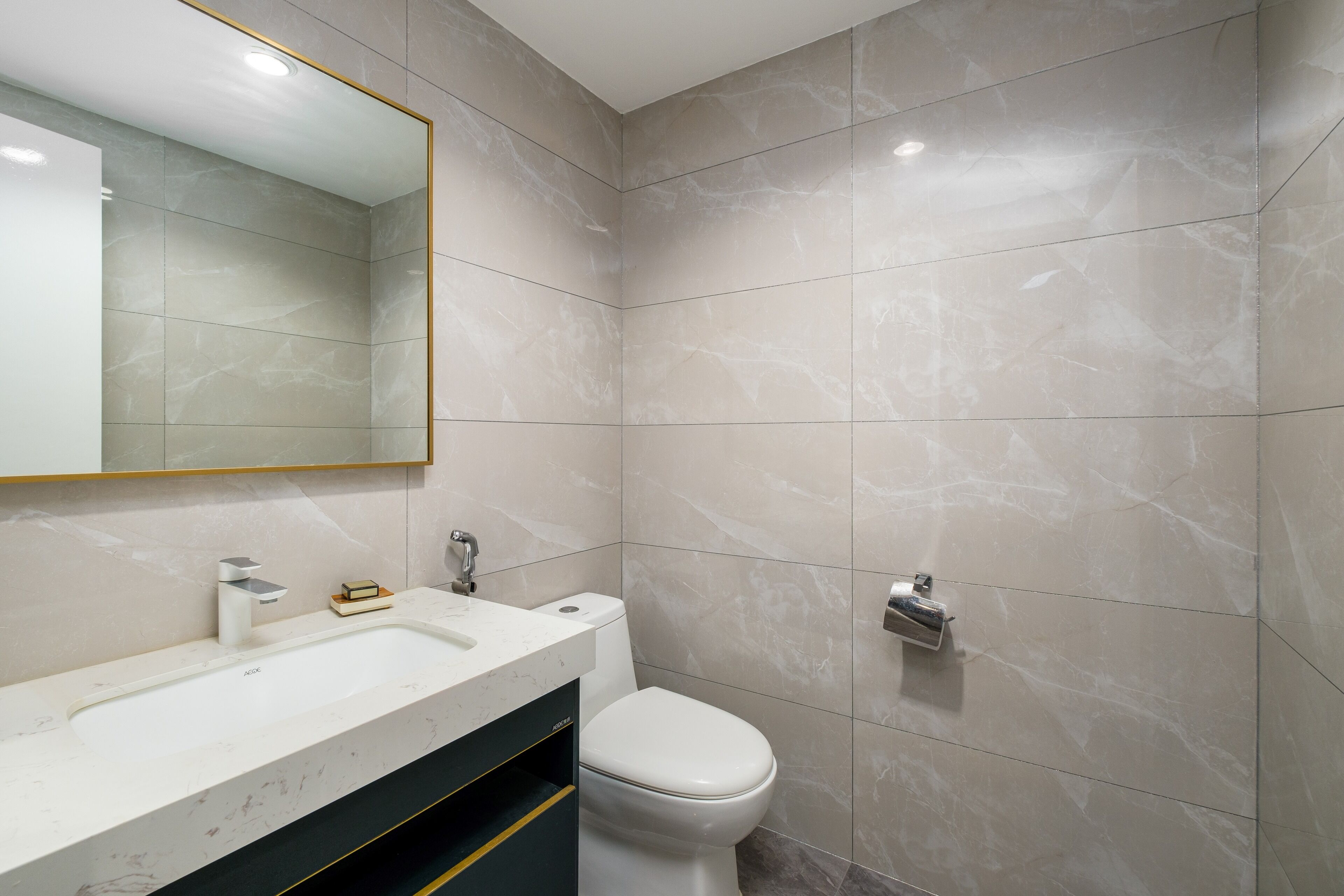Ein modernes Badezimmer mit Waschbecken, Toilette und Spiegel mit goldener Rahmung.