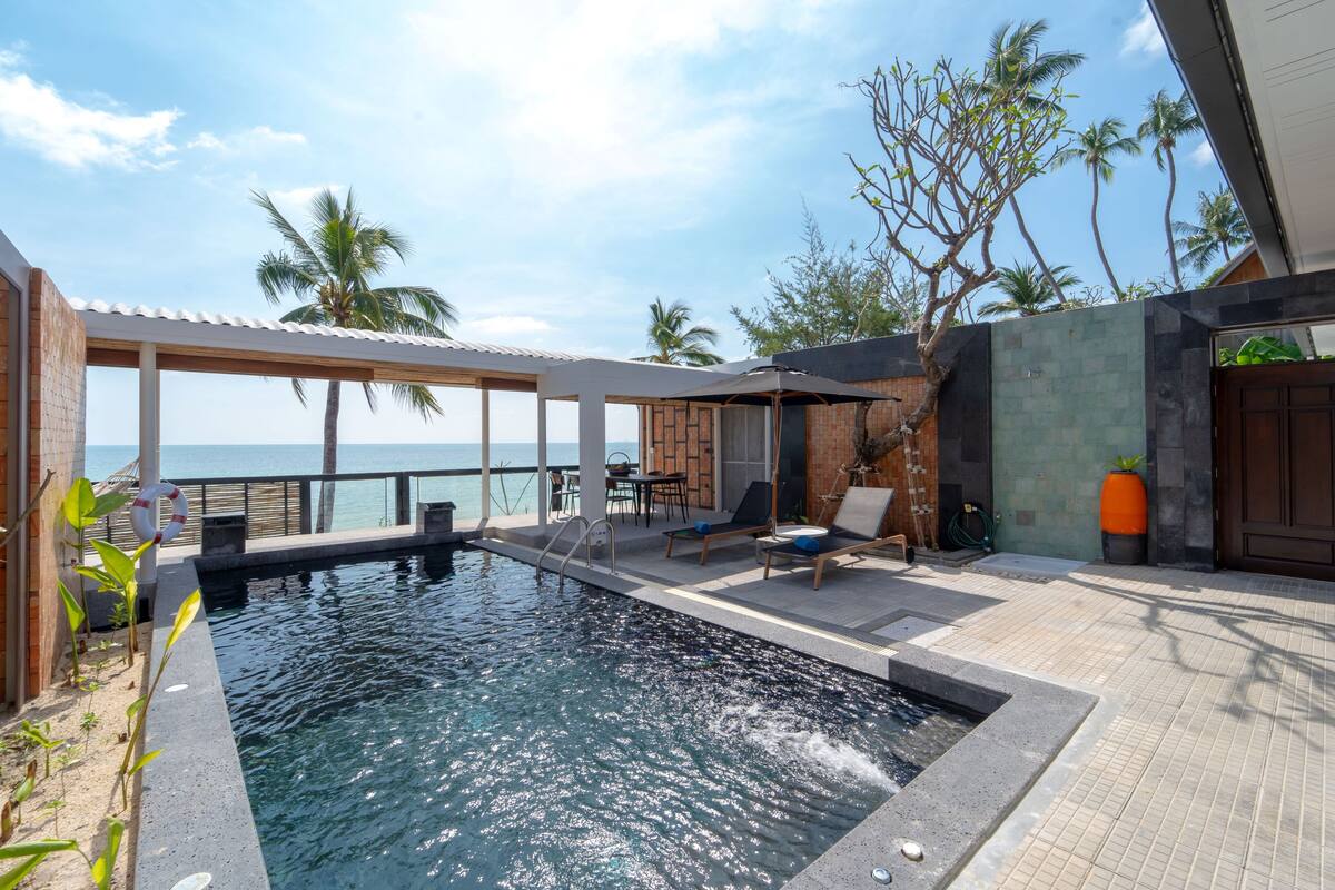 A pool area with a view of the ocean, lounge chairs, and a covered seating area.