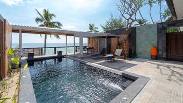 A pool area with a view of the ocean, lounge chairs, and a covered seating area.