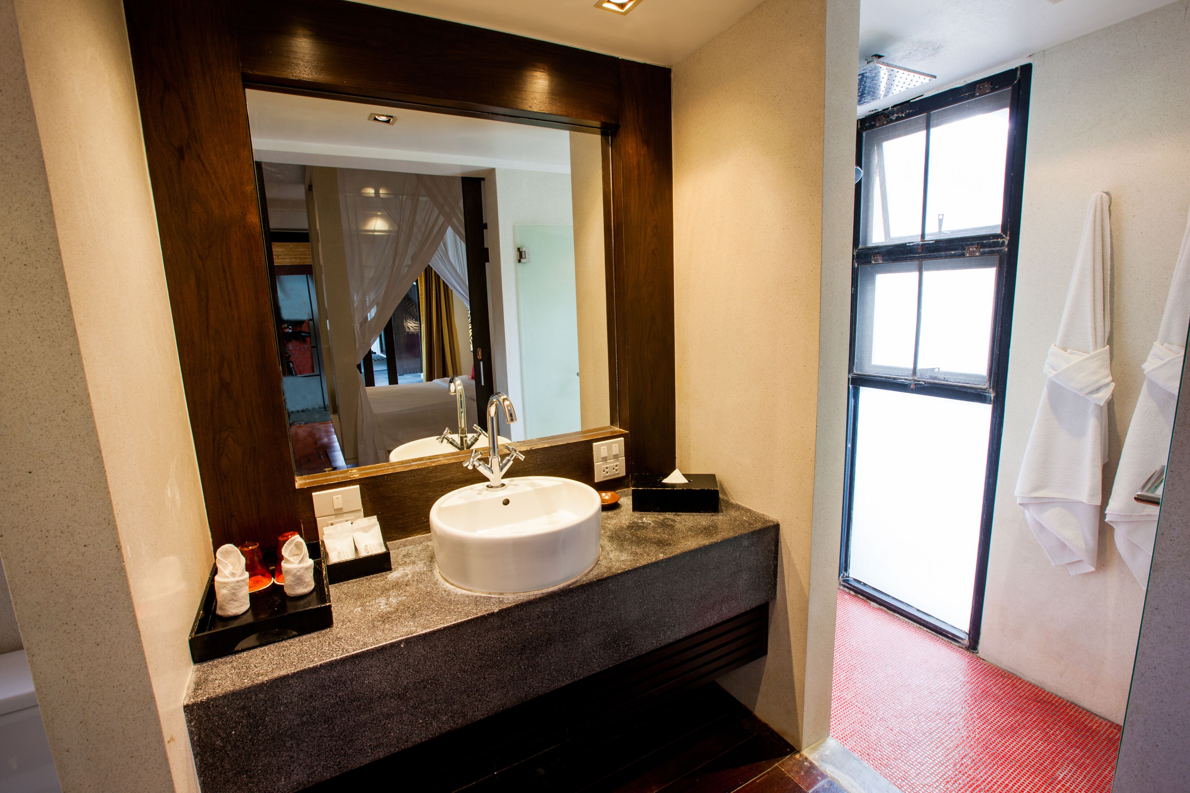 Un baño moderno con un espejo grande, un lavamanos blanco y un suelo de baldosas rojas.
