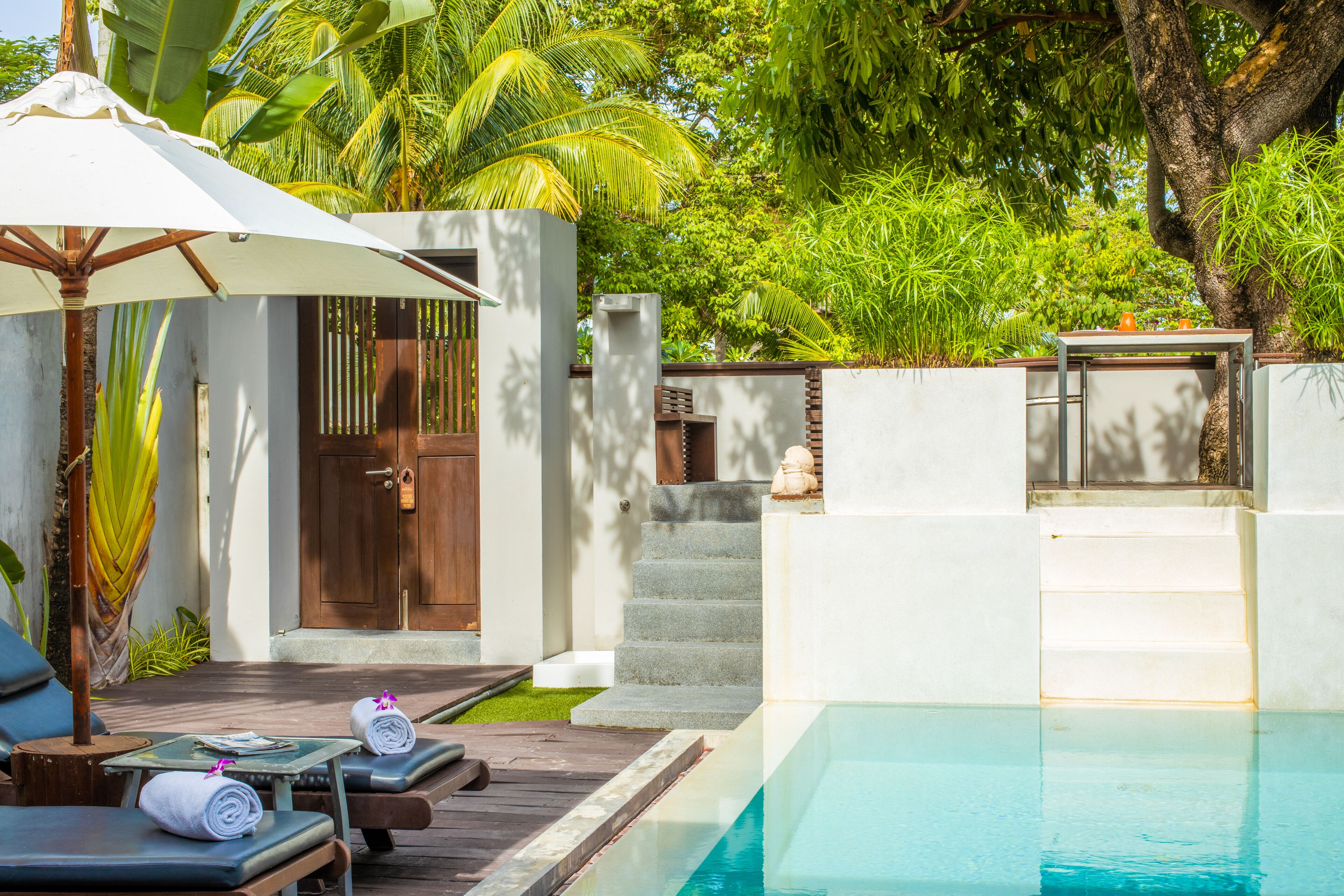 A poolside area with lounge chairs, a wooden deck, and a white umbrella.