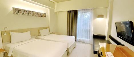 Une chambre d’hôtel avec deux lits, un bureau avec une télévision, une fenêtre avec des rideaux et une œuvre d’art accrochée au mur.
