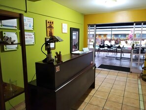 A reception desk with a computer, a no-smoking sign, and a glass door leading to an outdoor seating area. - Puerta del Sol (Ulloa)