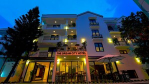 Un hotel de varios pisos con un balcón en el segundo piso, mobiliario exterior y un letrero que dice "The Dream City Hotel".