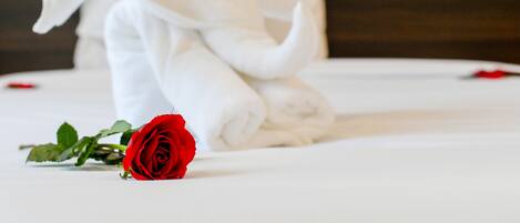 A neatly made bed with rolled towels and a single red rose.