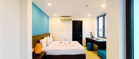 A modern hotel room with a large bed, a desk, and a window.
