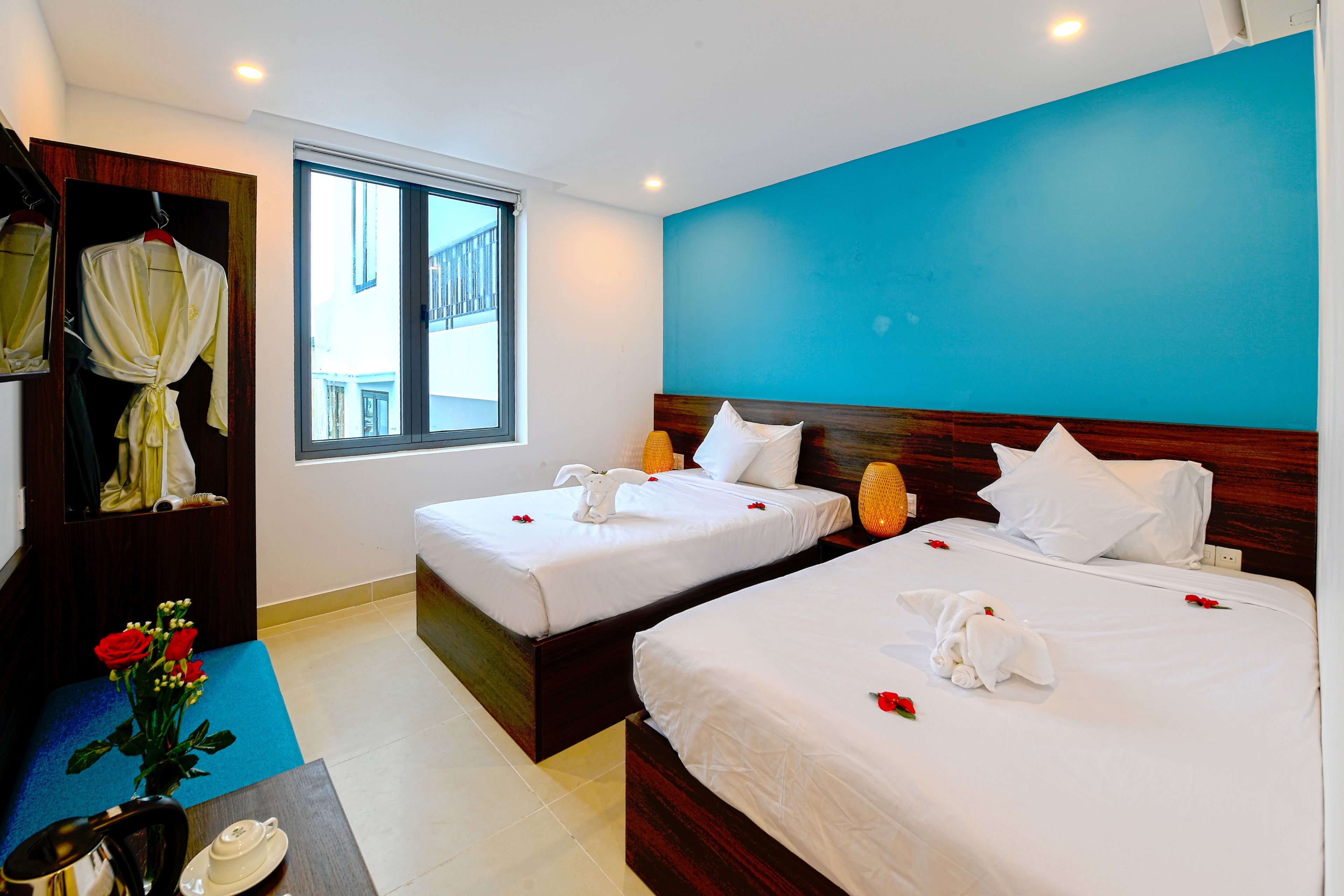 Een hotelkamer met twee bedden, een raam, een spiegel en een klein tafeltje met een bloevas.
