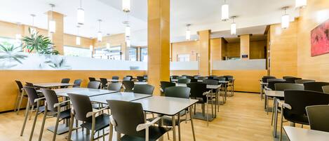 A modern dining area with multiple tables and chairs, wooden flooring, and pendant lighting.