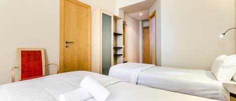A hotel room with two beds, a red chair, and a lamp.