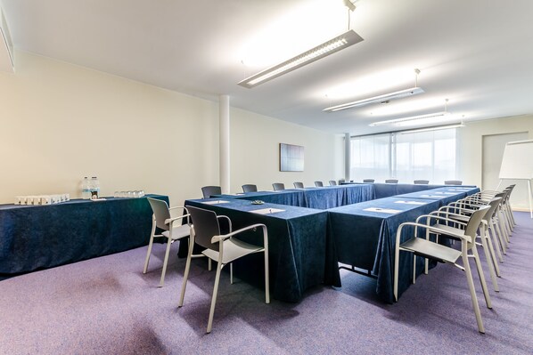 Un salón de conferencias con una larga mesa, sillas y una pantalla para proyector.