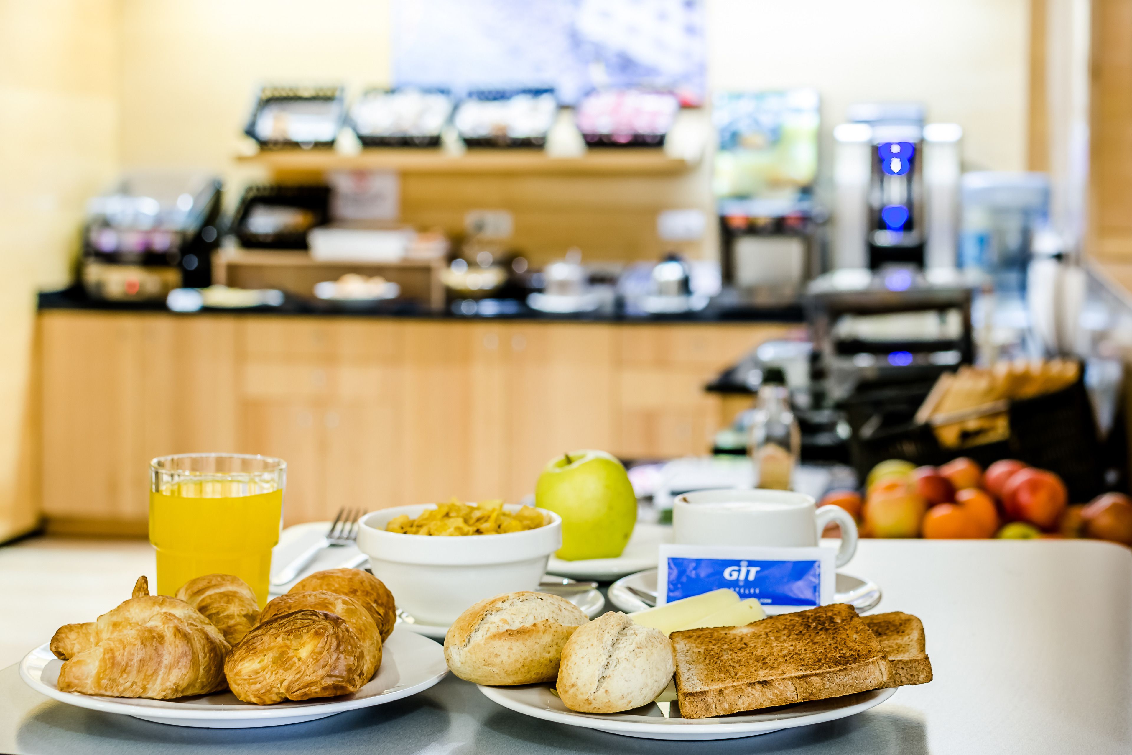 A breakfast setting with croissants, toast, a bowl of cereal, a glass of orange juice, and a cup of coffee on a table.