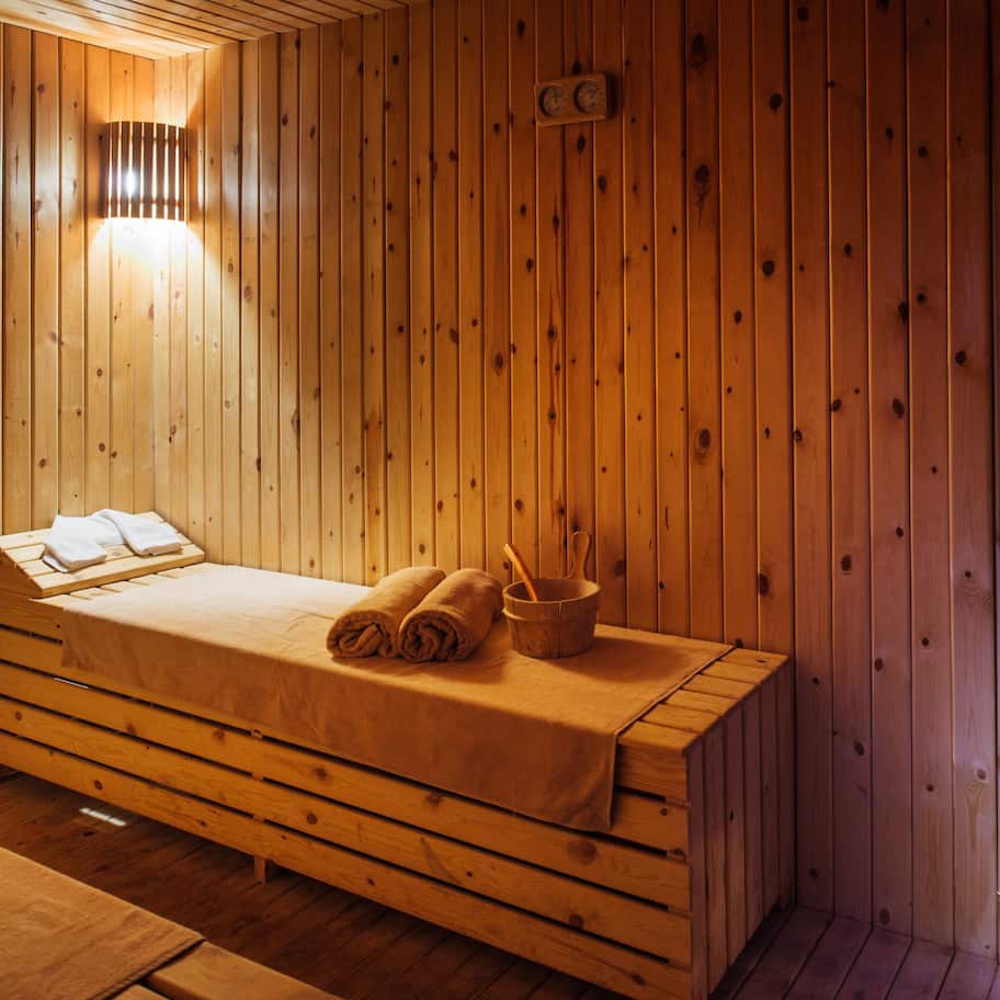 A wooden room with a bed, a bench, and a sauna.